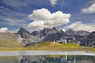 Bergsee im Hintergrund ist eine Bergbahnstation, Wolken, blauer Himmel und Berggipfel zu sehen